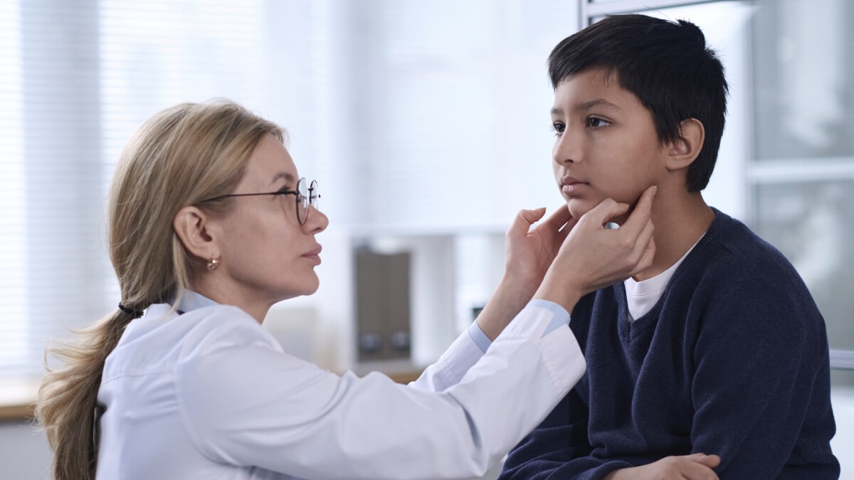 The image shows a clinician examining a child’s throat.