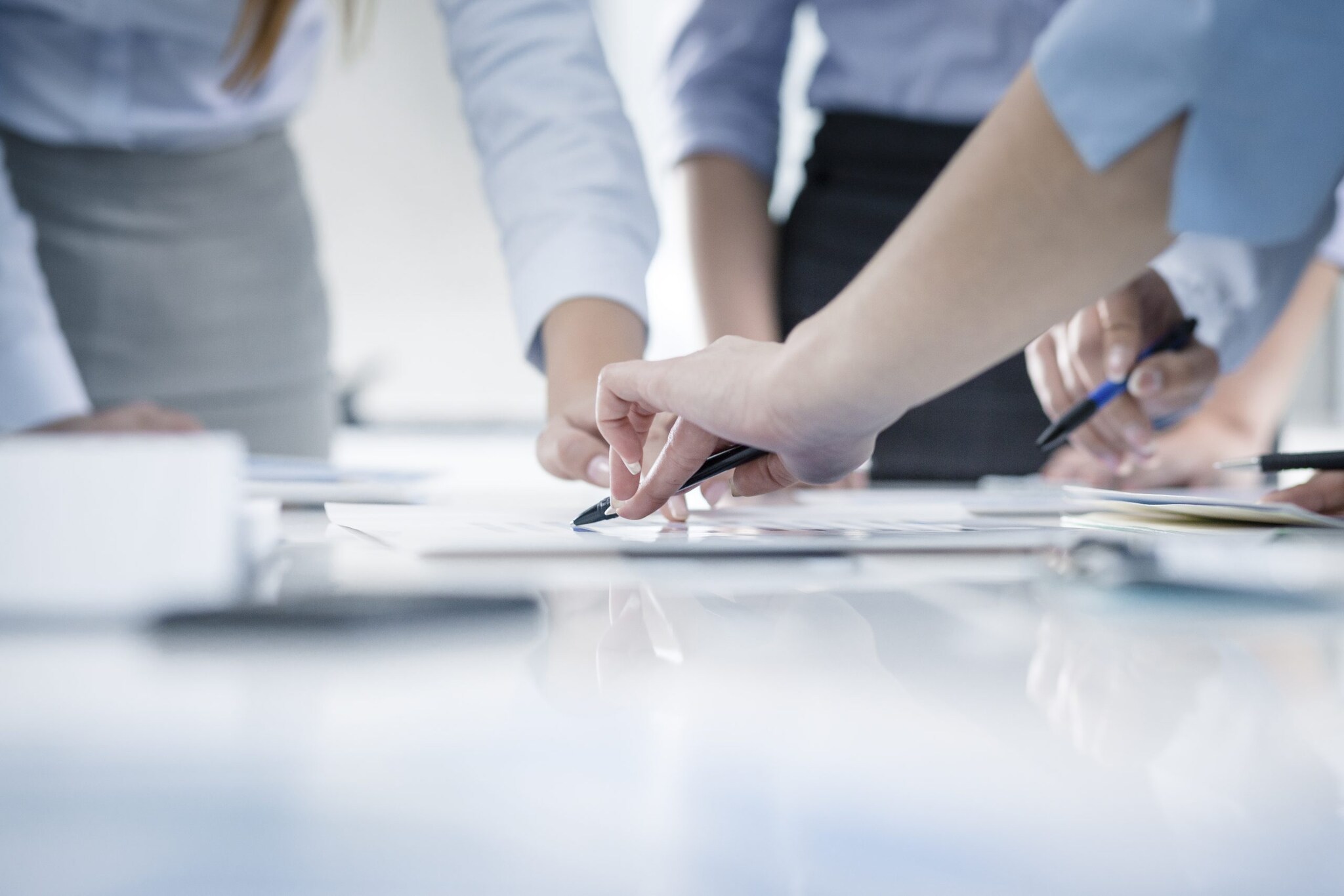 Group of people gathered around documents on a table with only their hands visible.