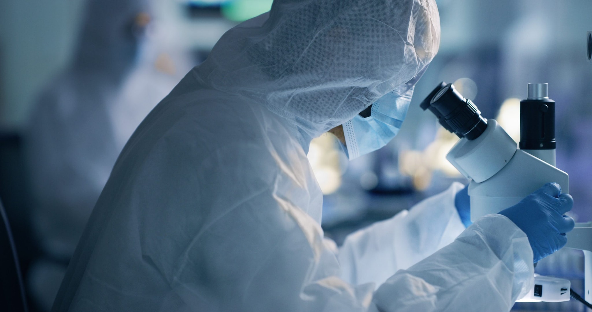 A laboratorian works at a microscope in full PPE