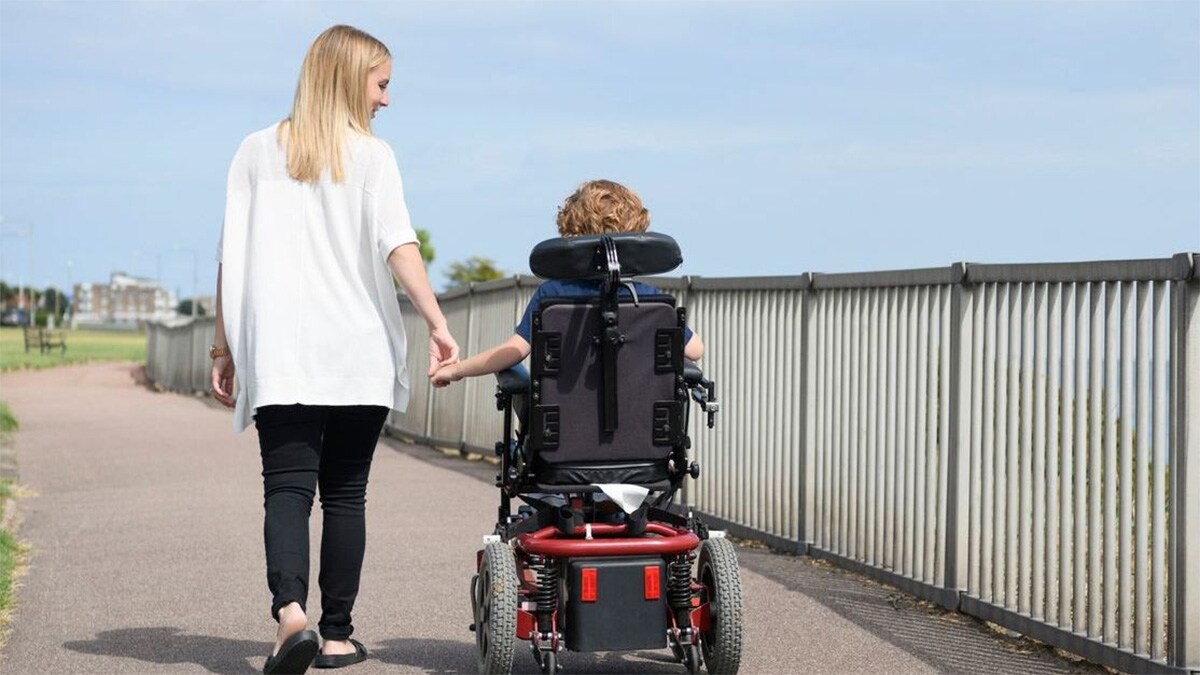 A mom holds hand and walks with her son in a wheelchair