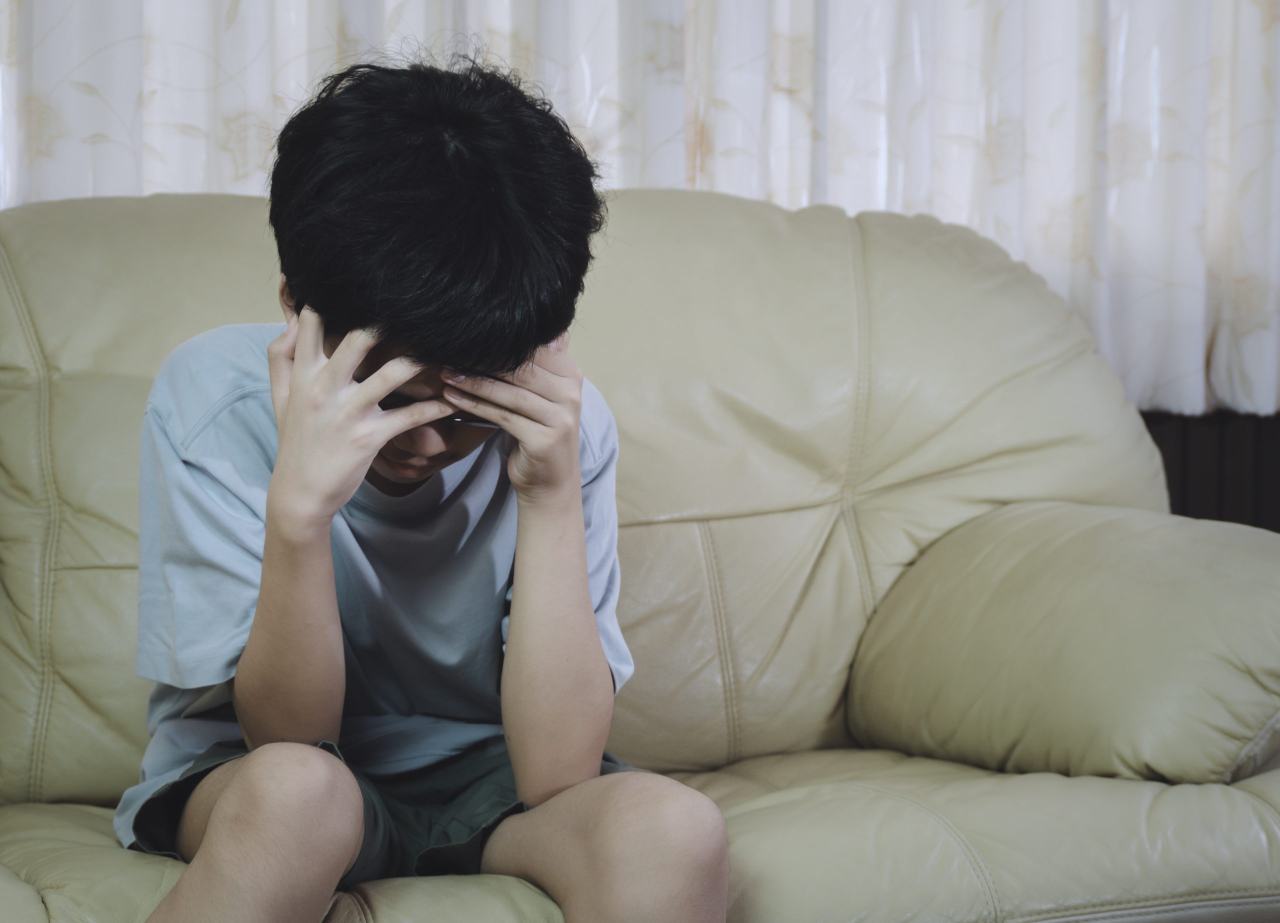 Un niño sentado en un sofá con la cabeza entre las manos.