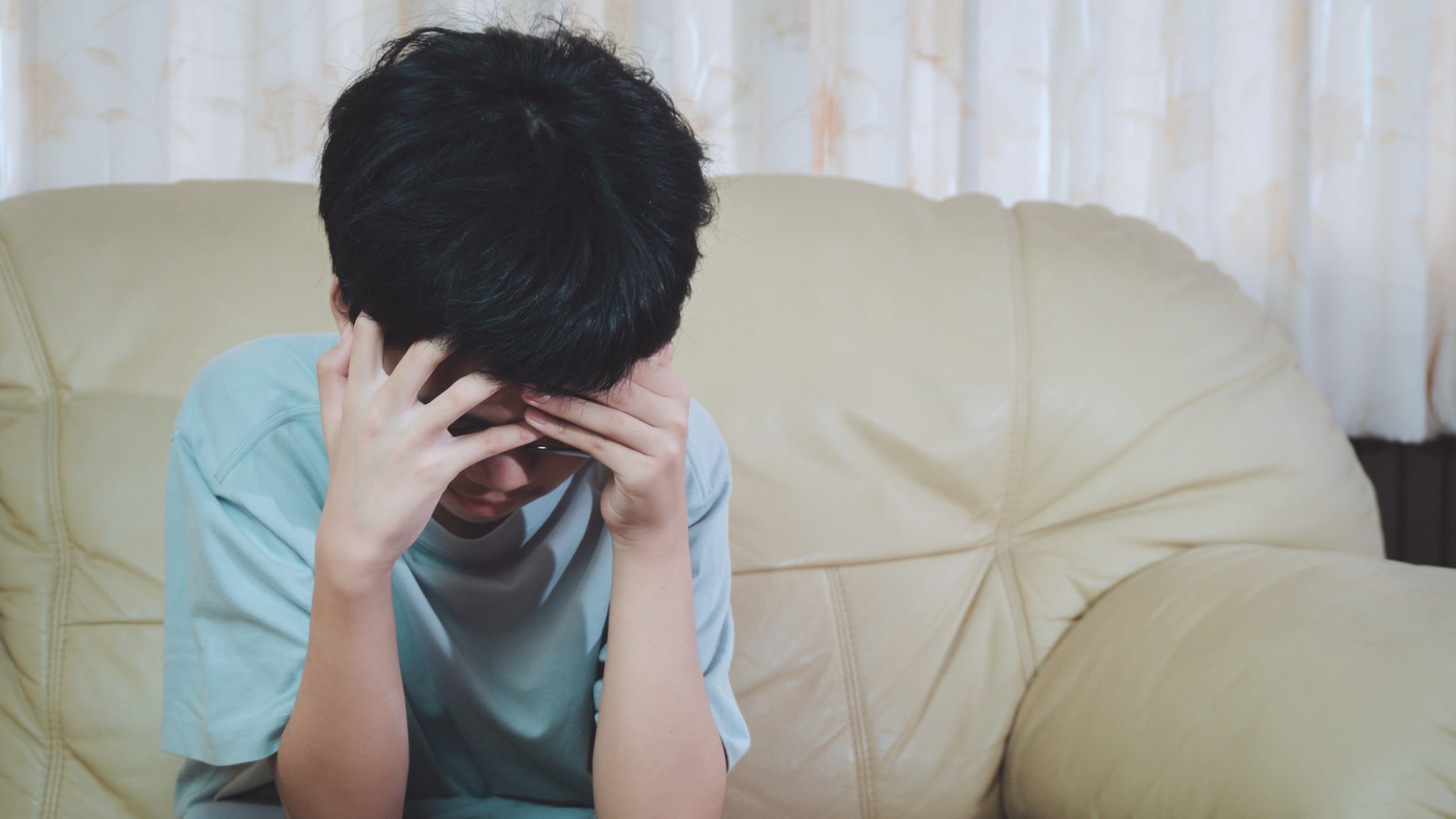 A young boy seated on a cough with his head in his hands.