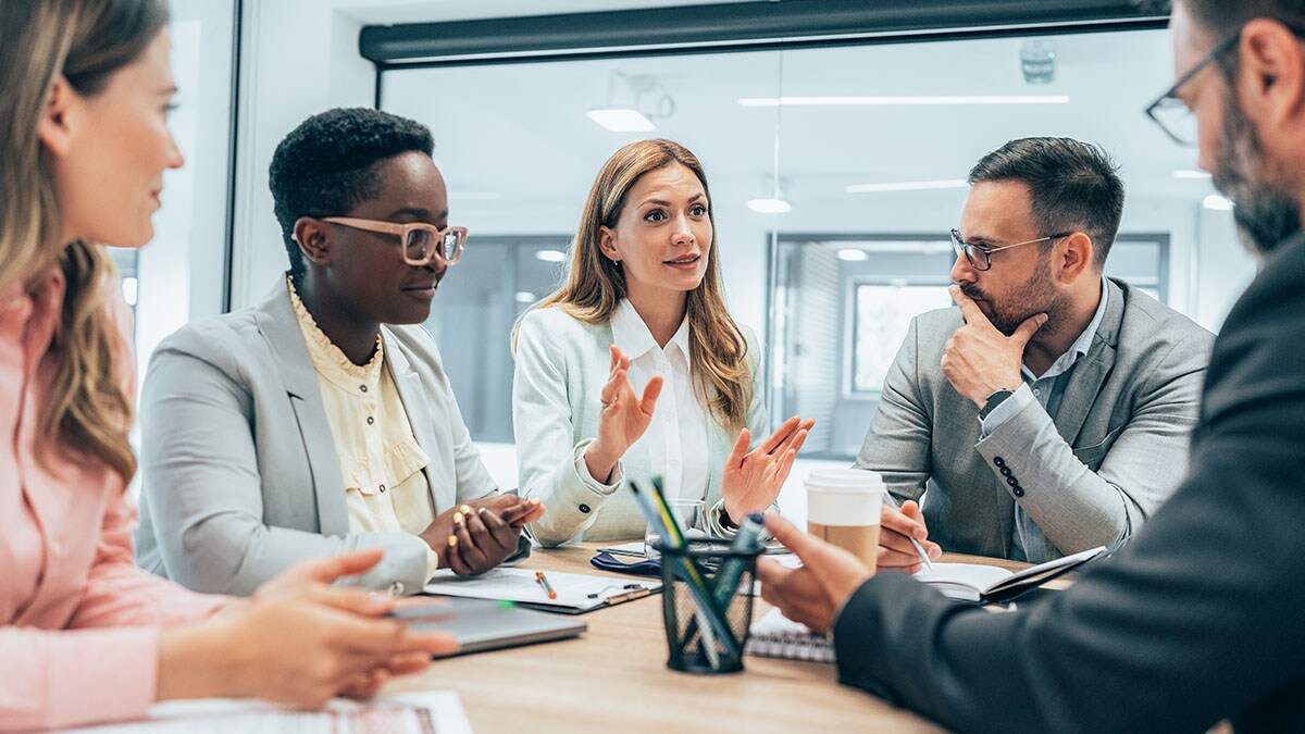 Five people at an office table talking