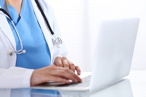 Doctor typing on laptop computer while sitting at the glass desk in hospital office