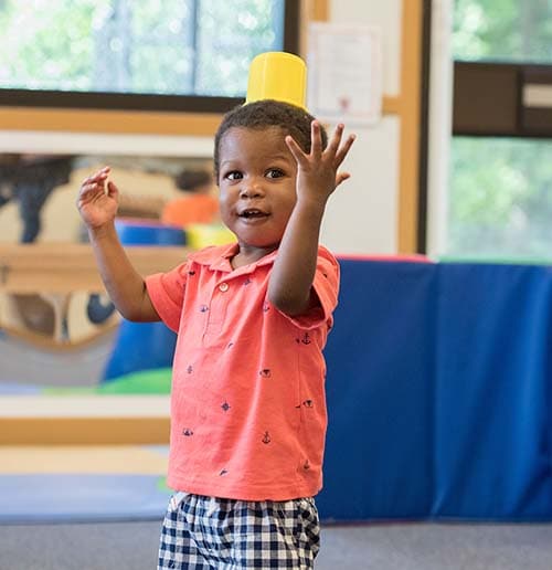 Boy with a cup on his head. Shows you what he can do by saying, “Look at me!”