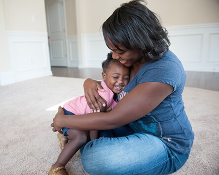 Mother holding her daughter while sitting on the floor