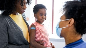 Mother with young son with Band-Aid on his arm sitting in exam room talking with doctor