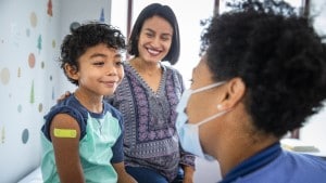 Young boy with Band-Aid on his arm sitting next to mother in exam room and smiling at doctor