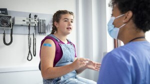 Teenage girl with bandaid on arm talking with doctor who is wearing a mask