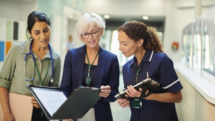 Two healthcare workers and an executive look at a folio together in a hospital hallway.