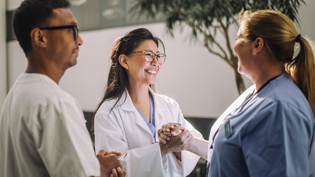 Two healthcare workers clasp hands in friendship while smiling.