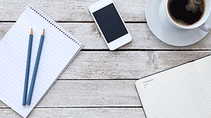 View of a desktop with a notebook, pencils, cell phone and cup of coffee