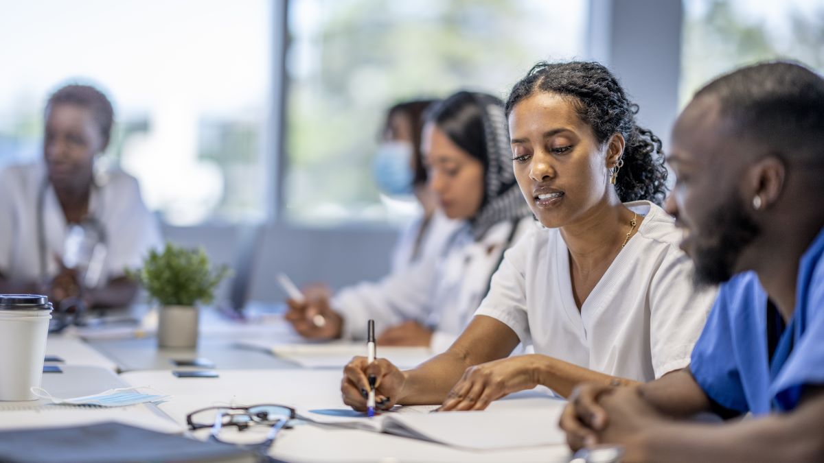 African American woman in scrubs collaborates with multicultural colleagues at conference table.