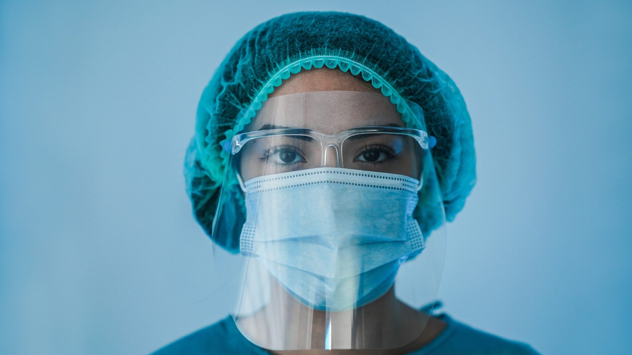 woman wearing hair cover, eye protection, and mask under a face shield