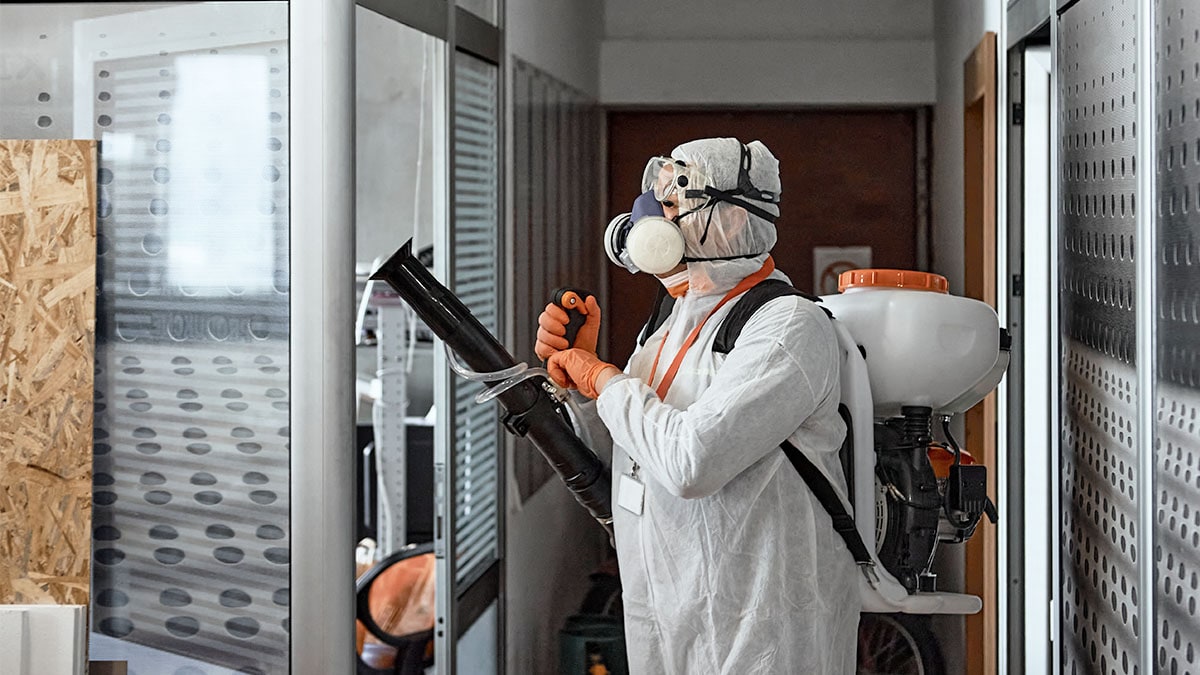 Man wearing a white  protective suit disinfecting a work space