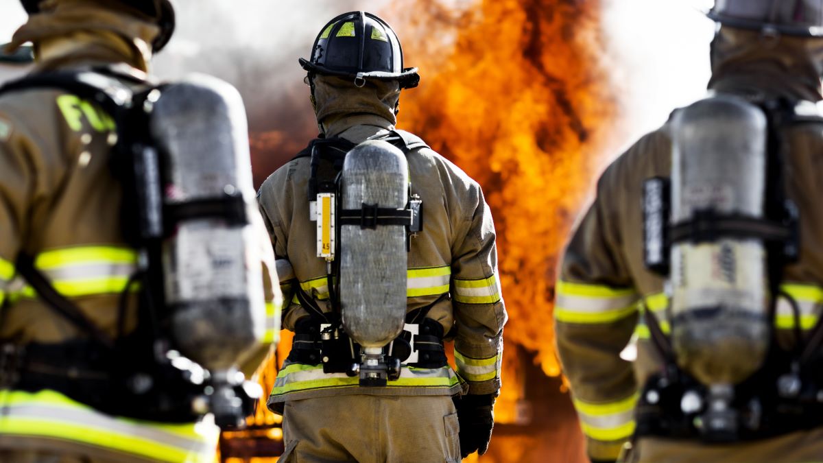 Three firefighters walking towards fire wearing self-contained breathing apparatus