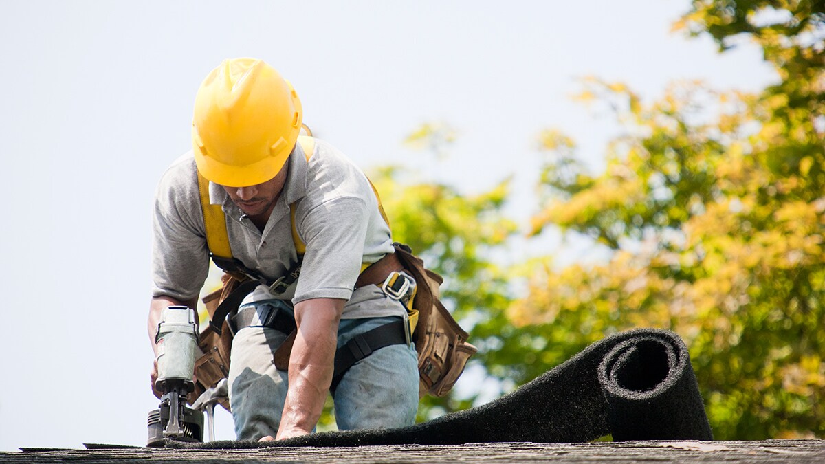 Roofer in safety gear nailing shingles into place.