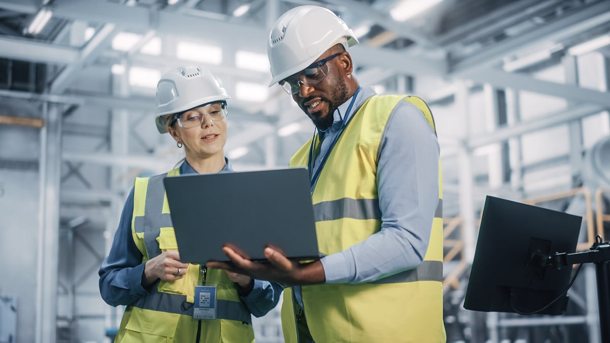 A male and female worker talking and looking at a laptop.