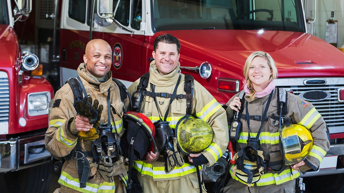 Group of structural firefighters standing in front of trucks with gear