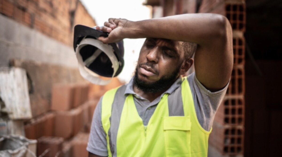 Worker wiping brow, showing signs of exhaustion.