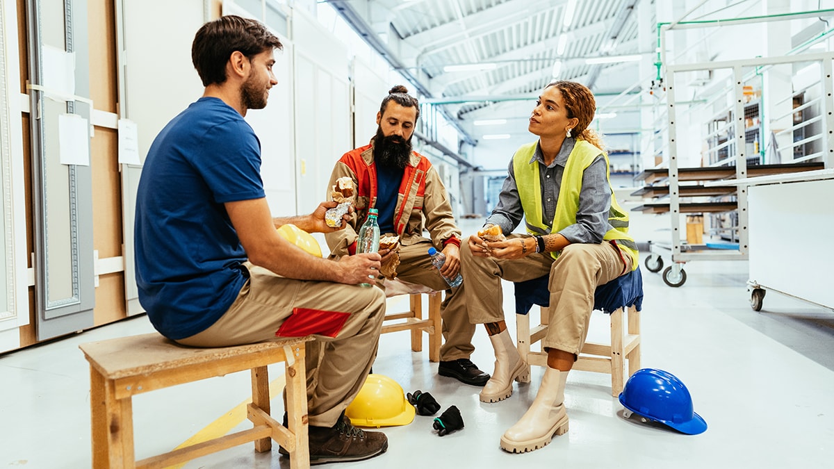 Three construction workers sit together, eating, and talking.