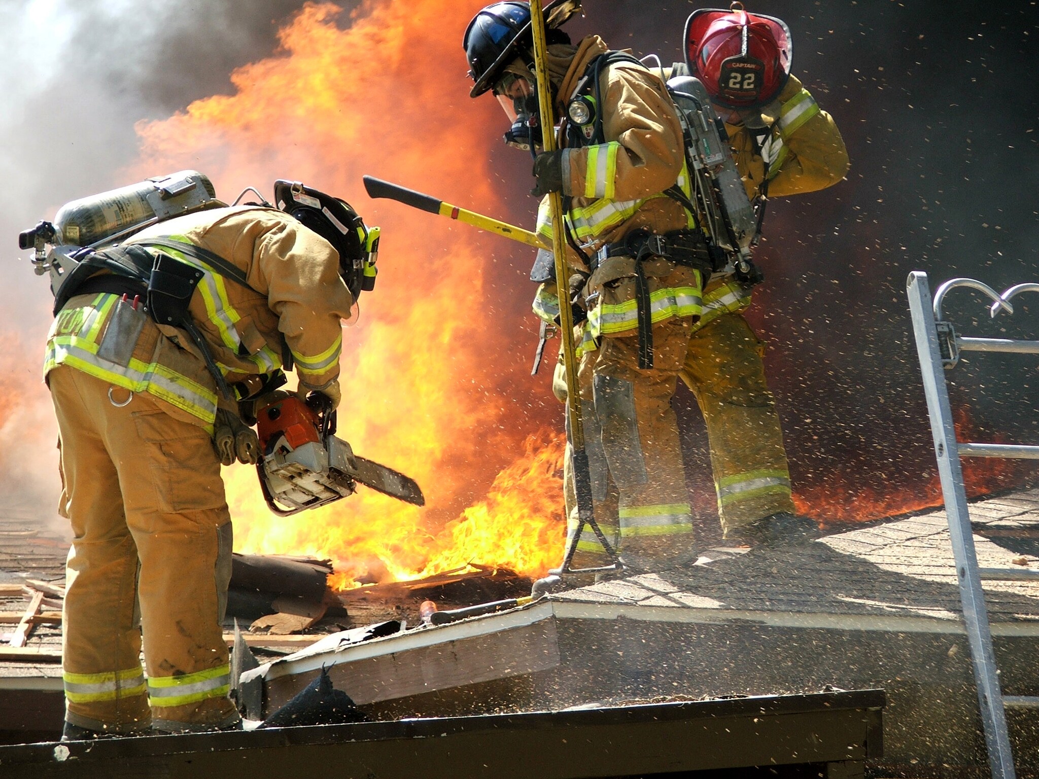 Bomberos usando EPP, llevando equipos, cerca de grandes llamas de fuego