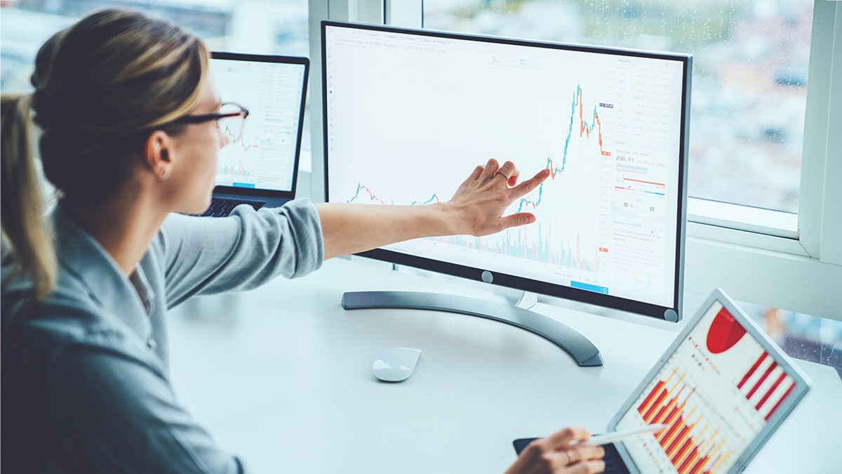 Woman in business attire pointing to graph on her computer monitor.