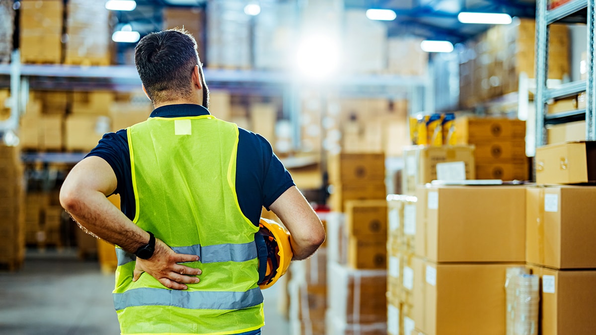 Warehouse worker in safety vest holding his lower back