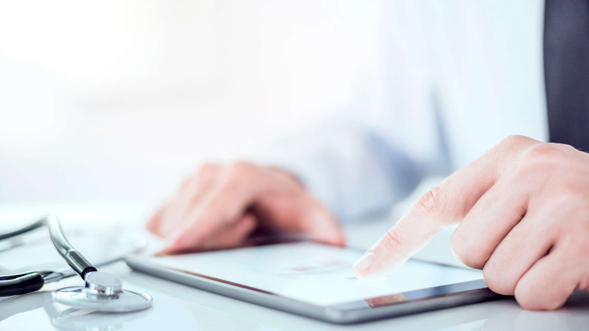 Close up of doctor looking at a digital tablet with a stethoscope lying beside the tablet.