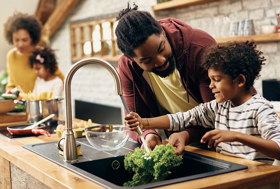 Father helps son wash vegetables.