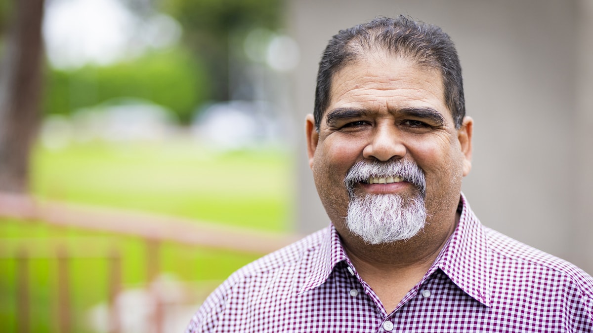 Portrait of an older, Hispanic man wearing a purple button-down shirt.