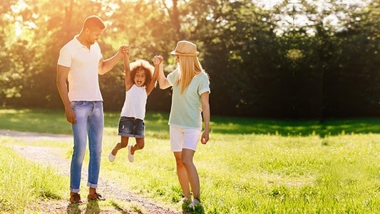 Couple with young child walking in a park on a sunny day.