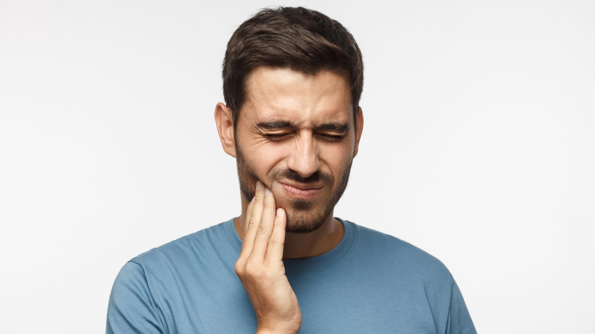 Adult male grimaces while touching jaw