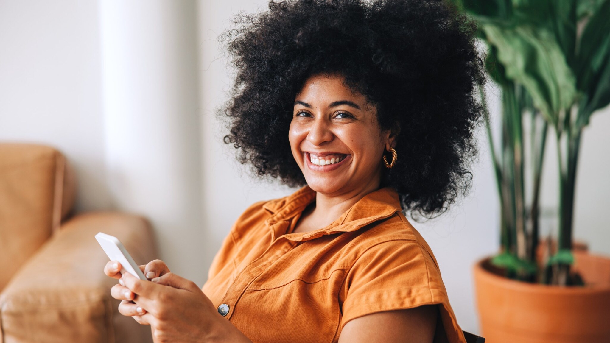 A young woman smiles while holding her smartphone.