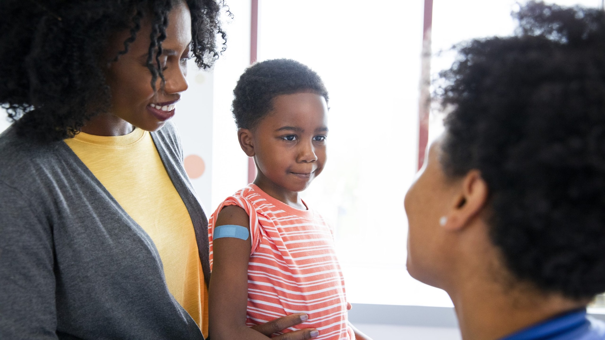 Child sitting on his mother's lap at the doctor with a bandaid on his arm from receiving a vaccination.