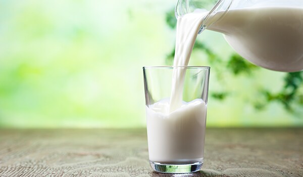 Pitcher pouring milk into a glass on a table.