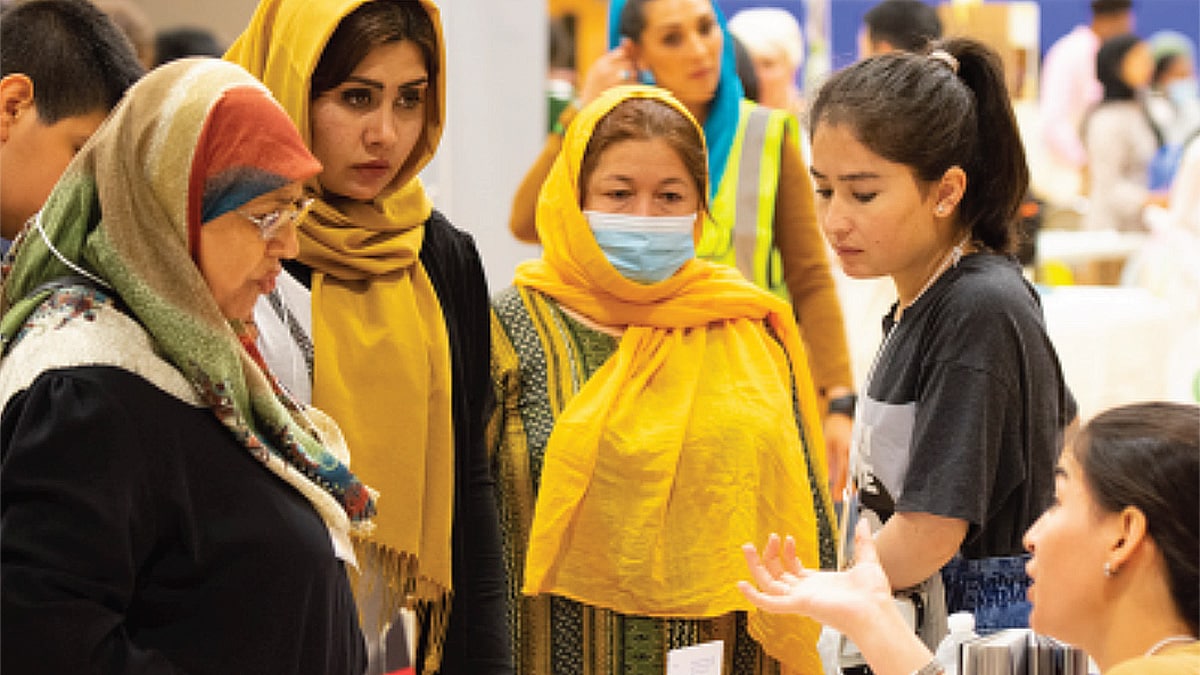 Women wearing hijabs are assisted by two young women at a gathering.