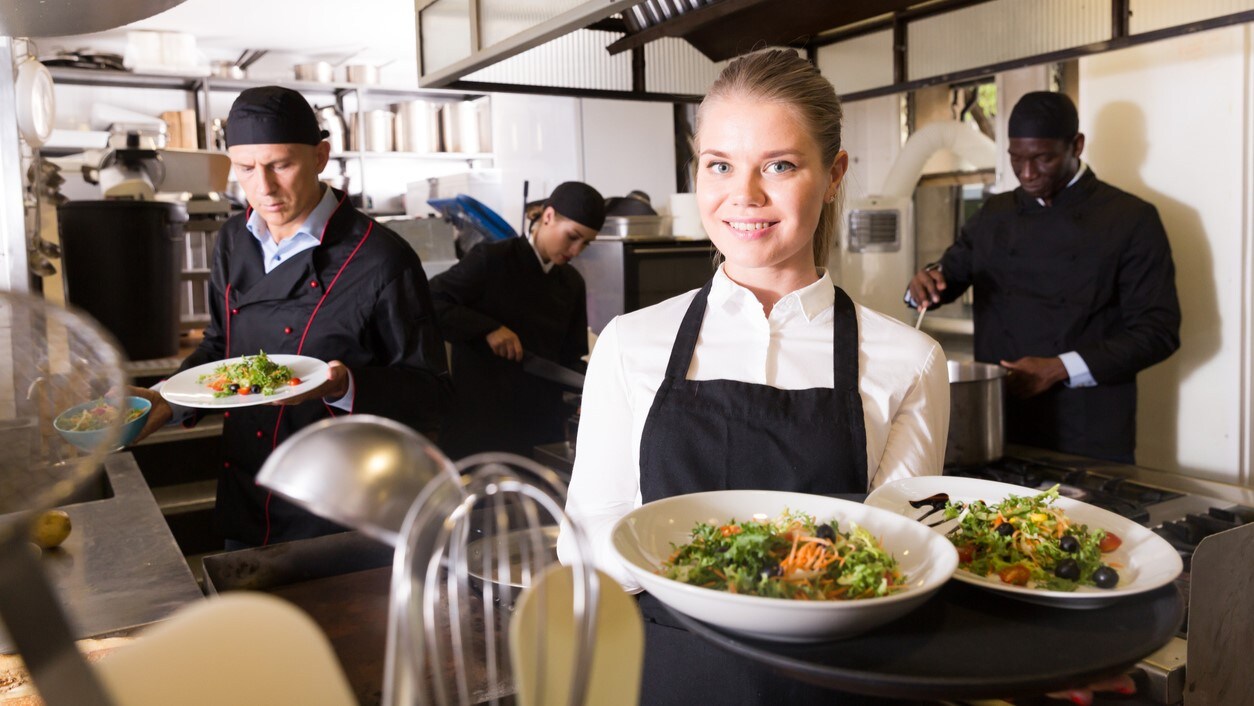 Food worker holding plates with a kitchen in the background.