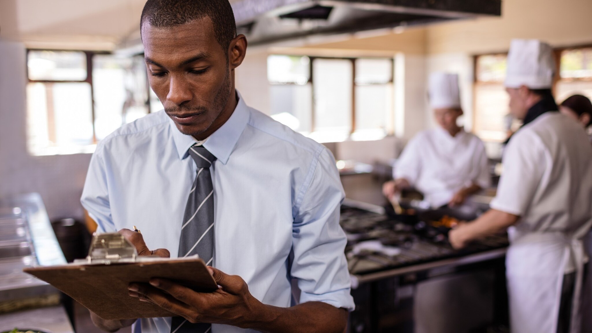 Investigator in the foreground writing on a clipboard with chefs in the background.