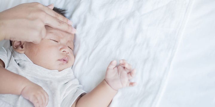 mother checking temperature with 2 fingers on baby's forehead