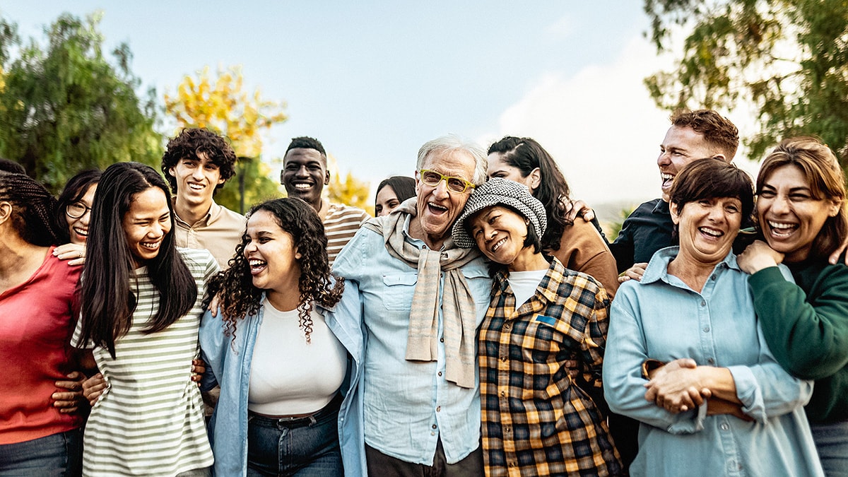 Multigenerational, diverse group of adults embracing each other in a park.