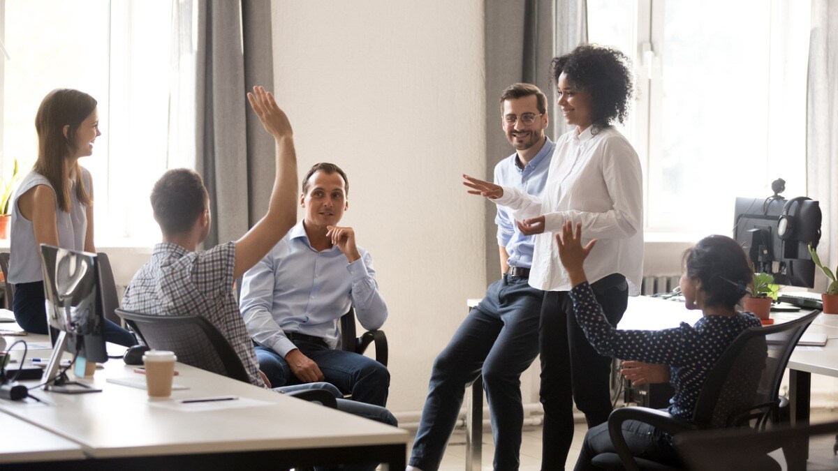 Five coworkers talking and sharing ideas at work. One person is raising their hand.