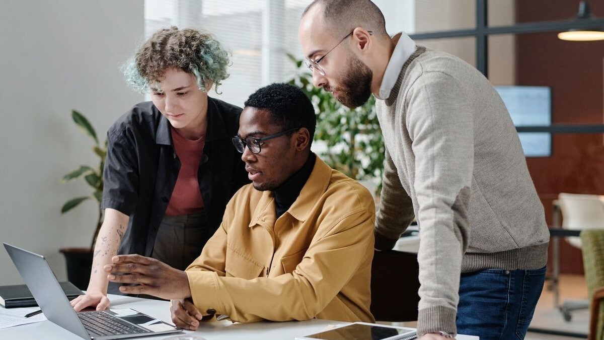 Three coworkers looking at a laptop at a desk.