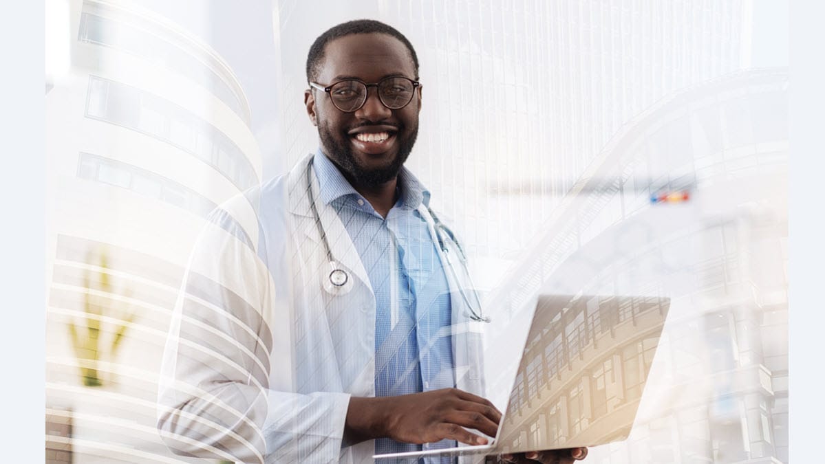 A smiling health care provider holds a laptop computer.