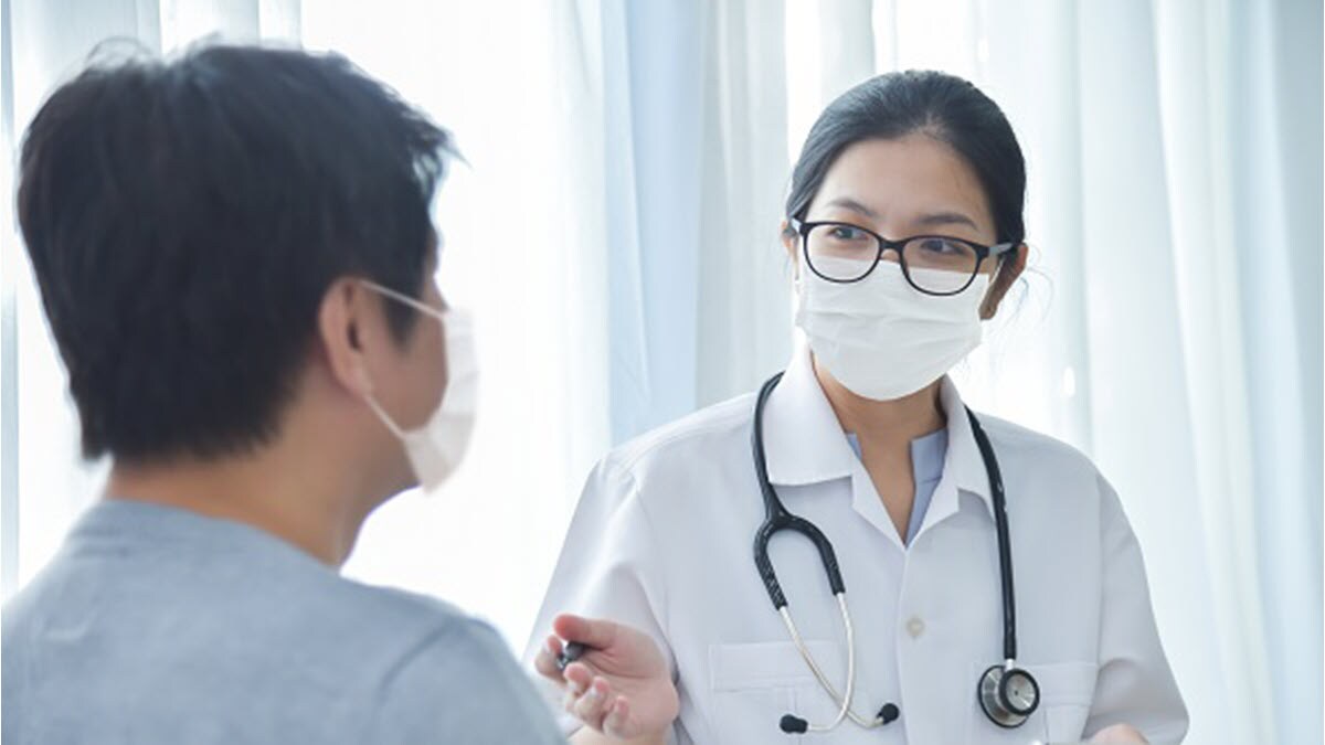 Female doctor talking to a male patient and both are wearing masks