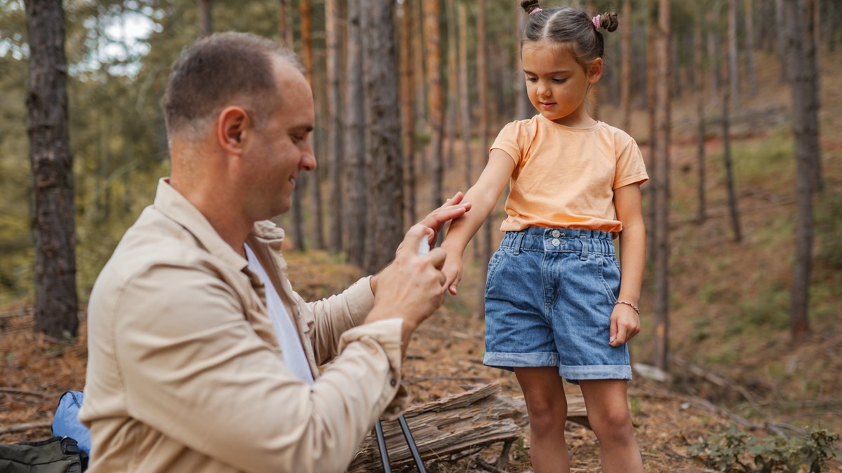 A father sprays tick repellent on his young daughter's arm for a forest hike.