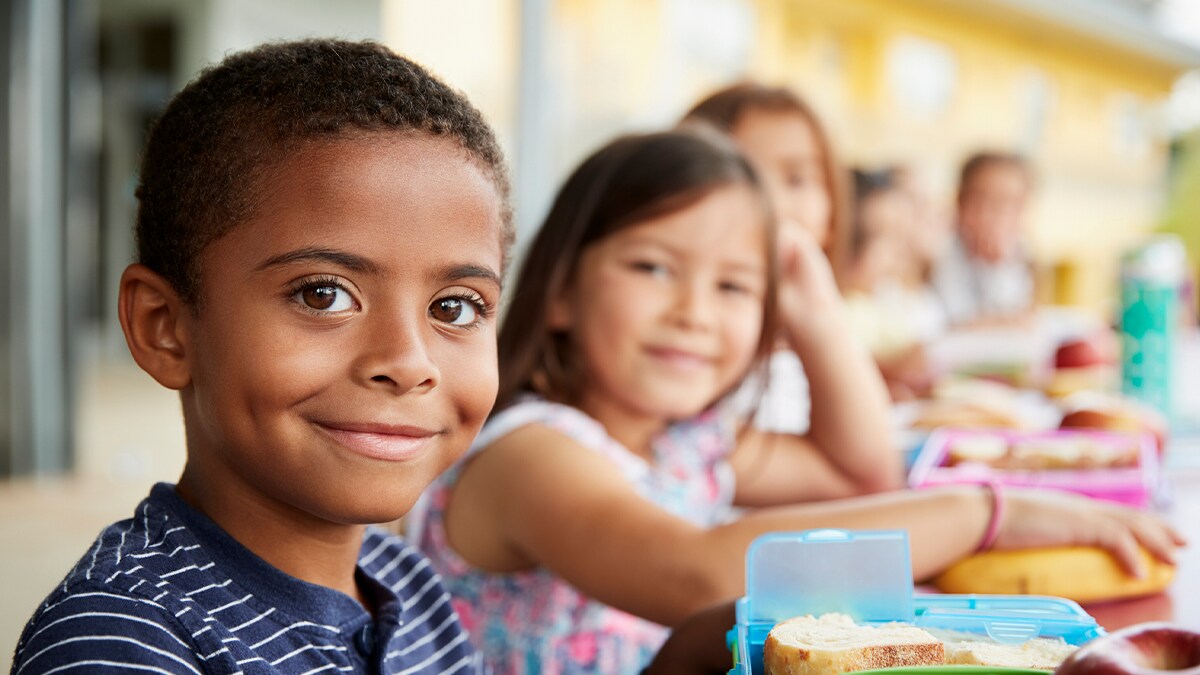 Young boy and girl at school lunch table smiling to camera