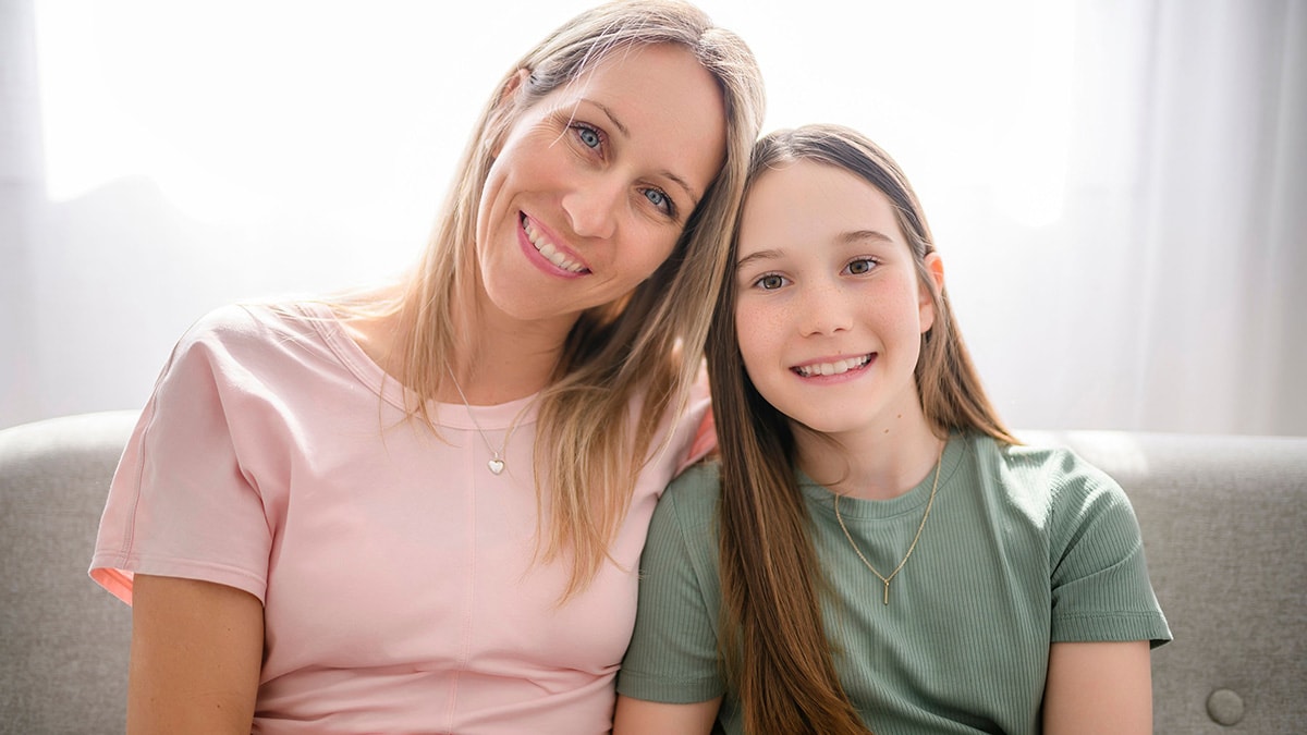 Mom stands behind her daughter, hugging her.