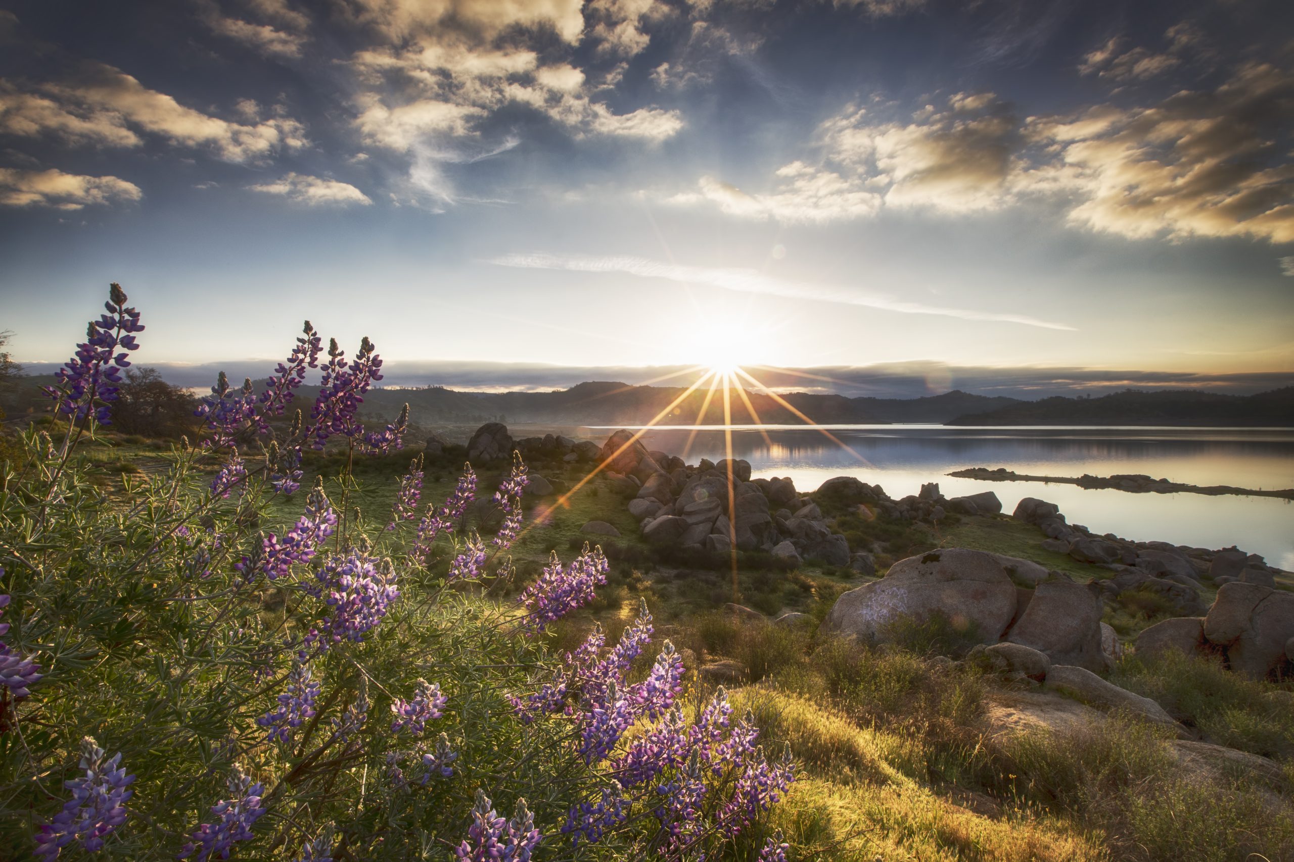 GettyImages-534415334.jpg A sunbeam shining over a landscape of mountains, water, rocks, and flowers