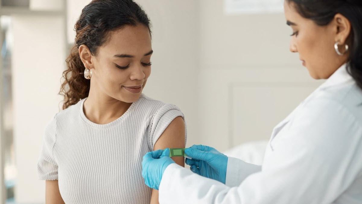 A healthcare professional applying a bandage to a patient’s upper arm after administering a vaccine.